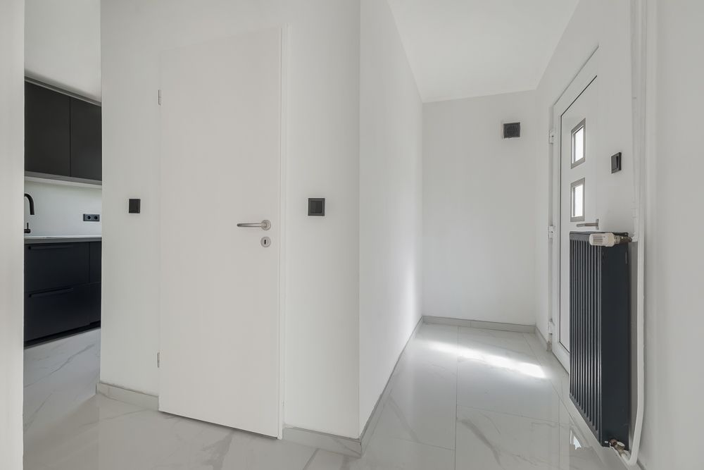 Heller Flur mit weißer Tür, Heizung und Blick in eine moderne schwarze Küche.