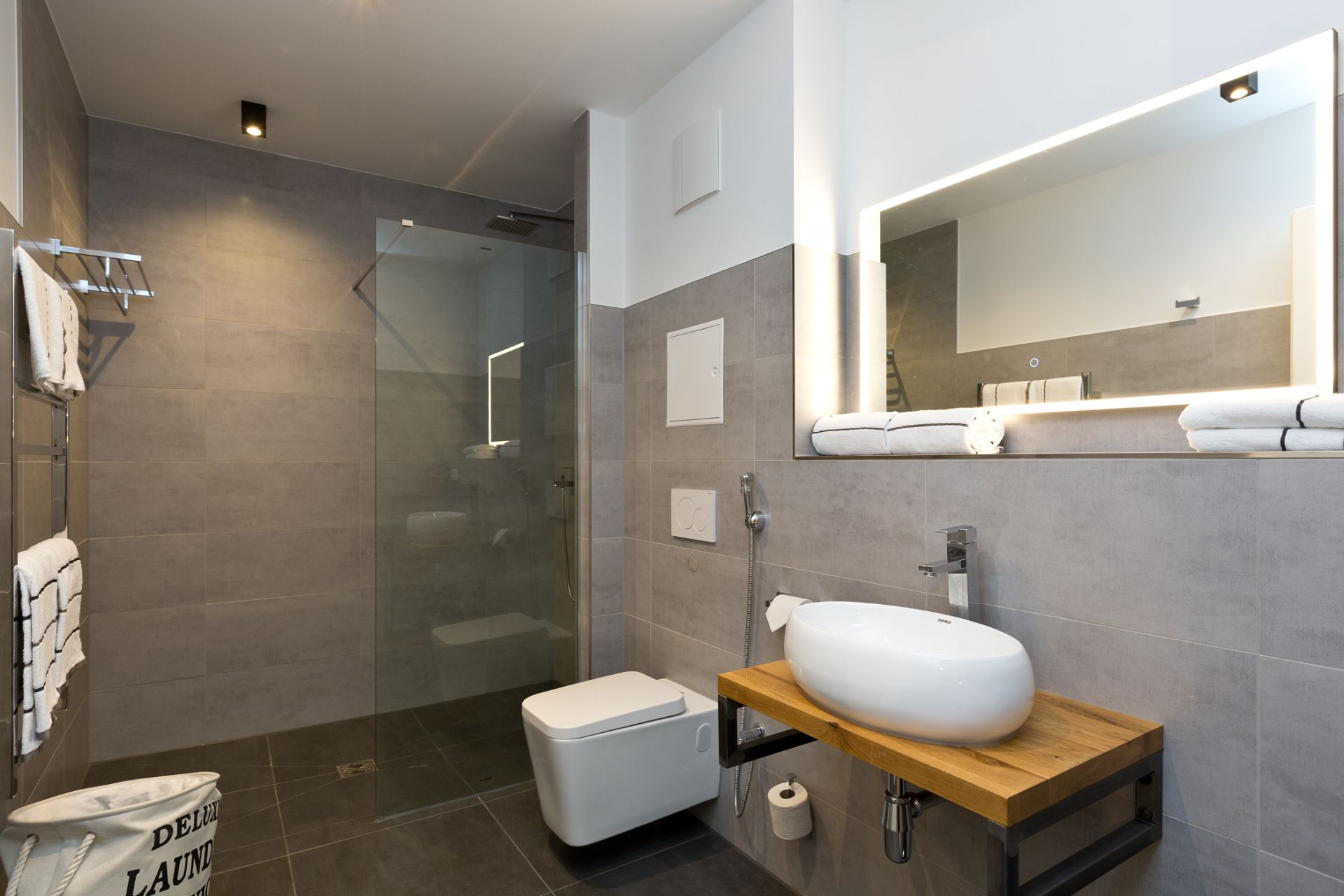 Modernes Bad mit begehbarer Dusche, Waschbecken, WC und großem beleuchtetem Spiegel.