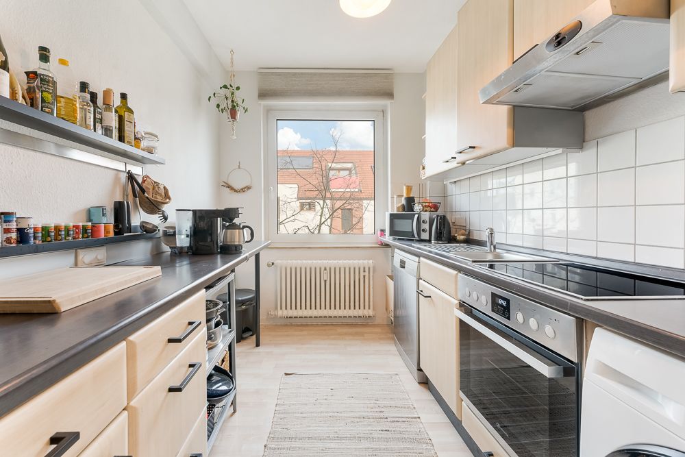 Helle, schmale Küche mit modernen Geräten, Holzfronten und einem Fenster am Ende des Raumes.