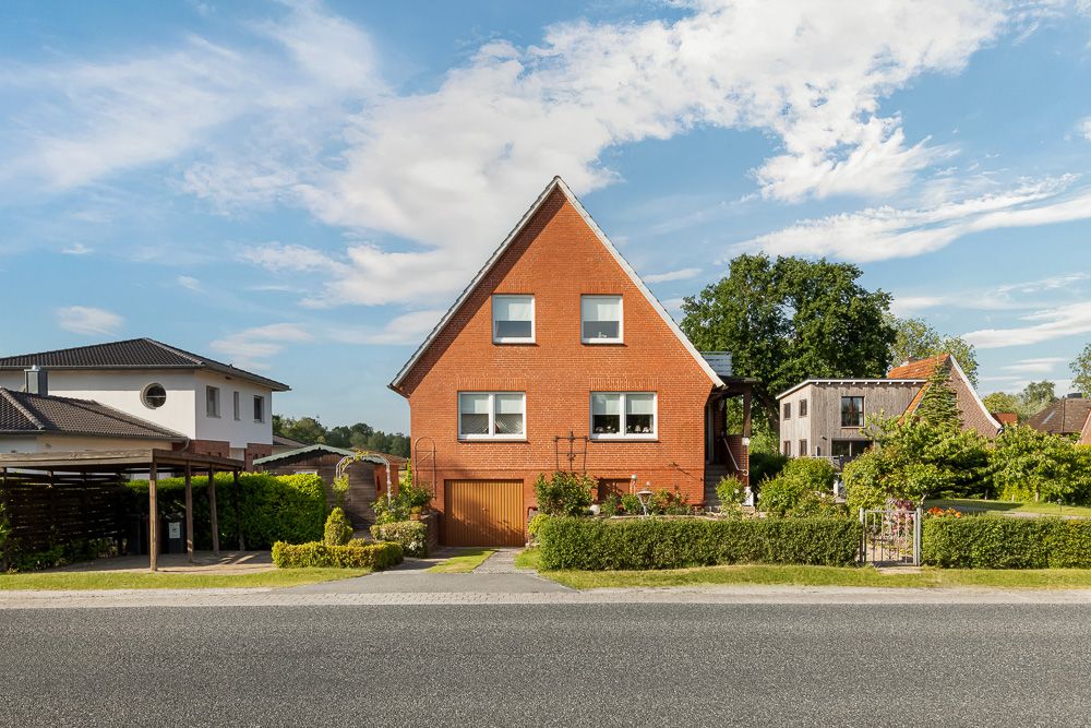 Ein rotes Backsteinhaus mit Satteldach und Garten, aufgenommen von der Straße.