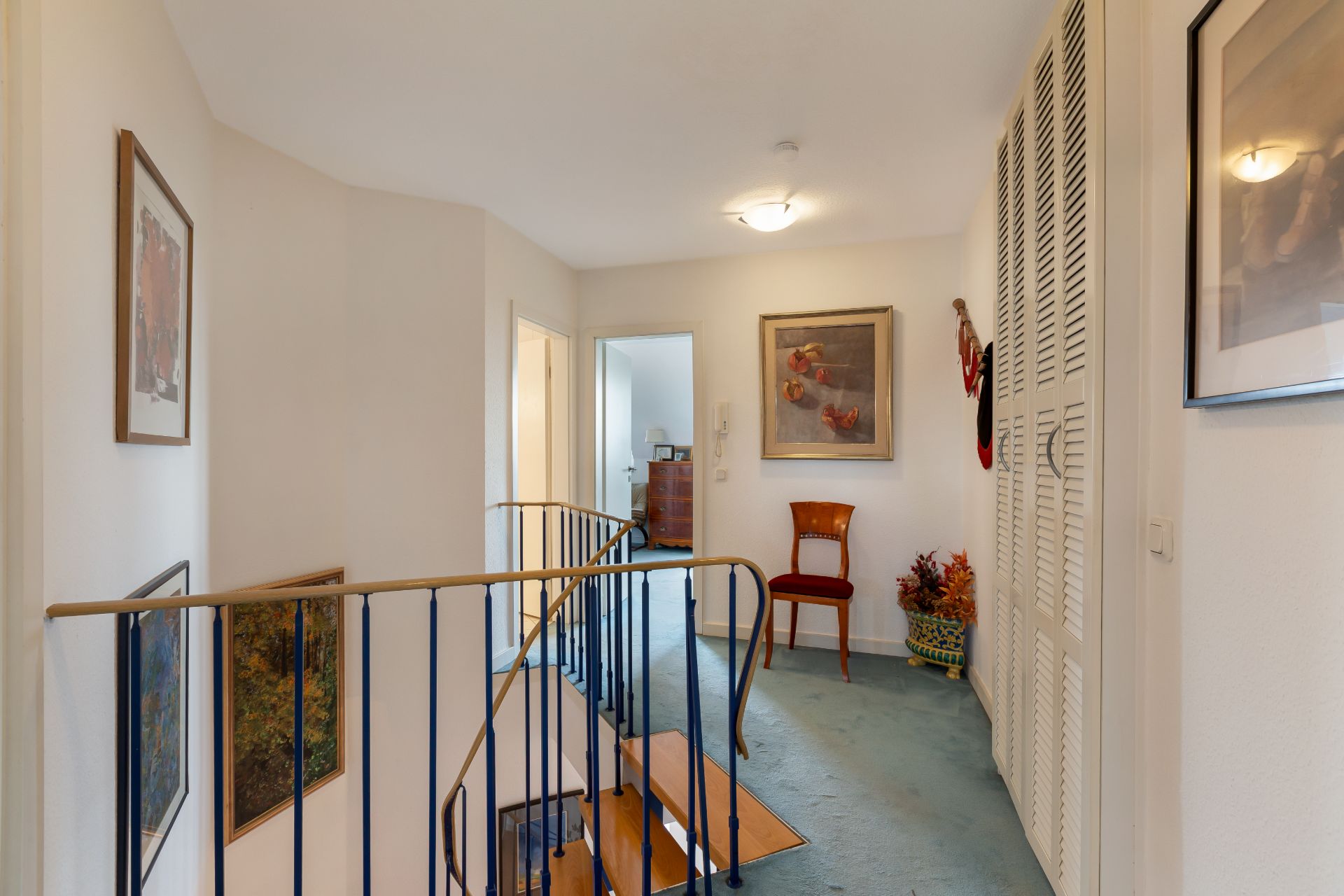 Heller Flur mit Treppe, Stuhl, Bildern an den Wänden und weißen Einbauschränken.