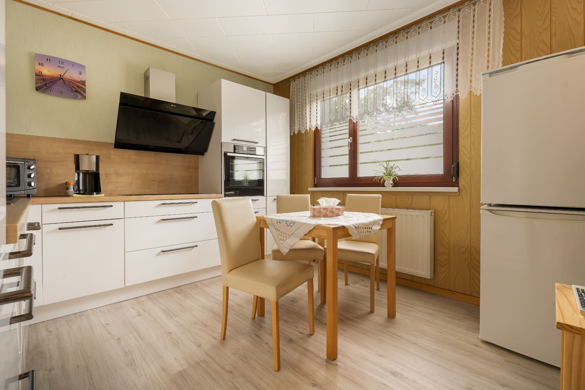 Helle Küche mit Esstisch, vier Stühlen, großen Fenstern und modernen Geräten.
