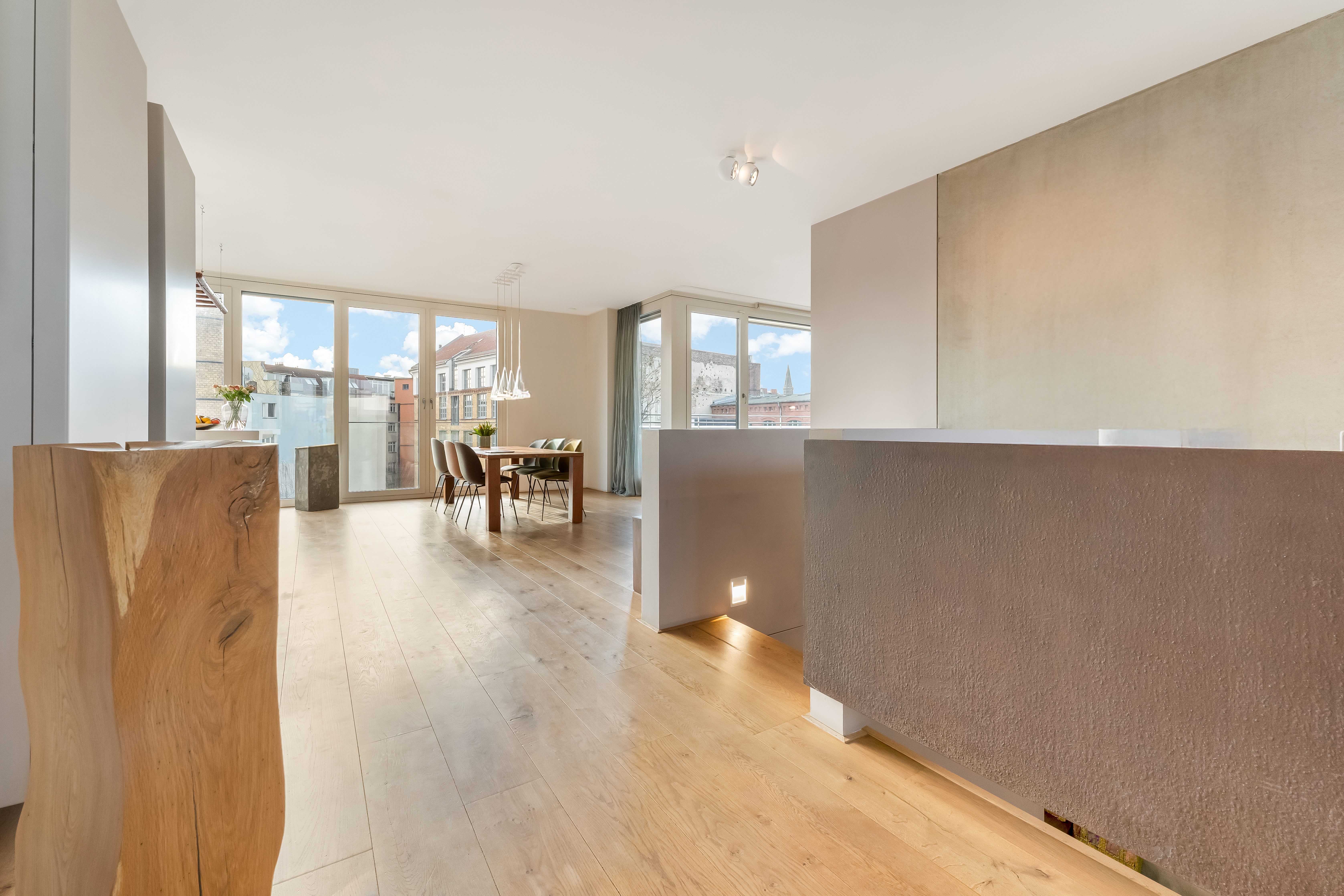 Helles Wohnzimmer mit Holzboden, Esstisch, großen Fenstern und Blick nach draußen.