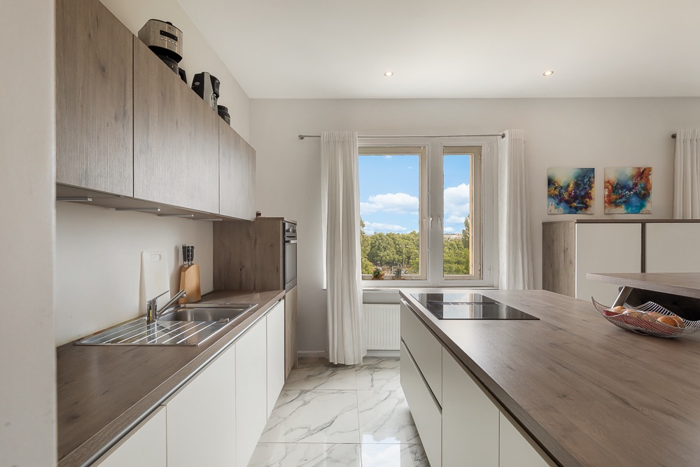 Moderne Küche mit Holzarbeitsplatten, Herdinsel, Fenster mit Ausblick und weißen Vorhängen.