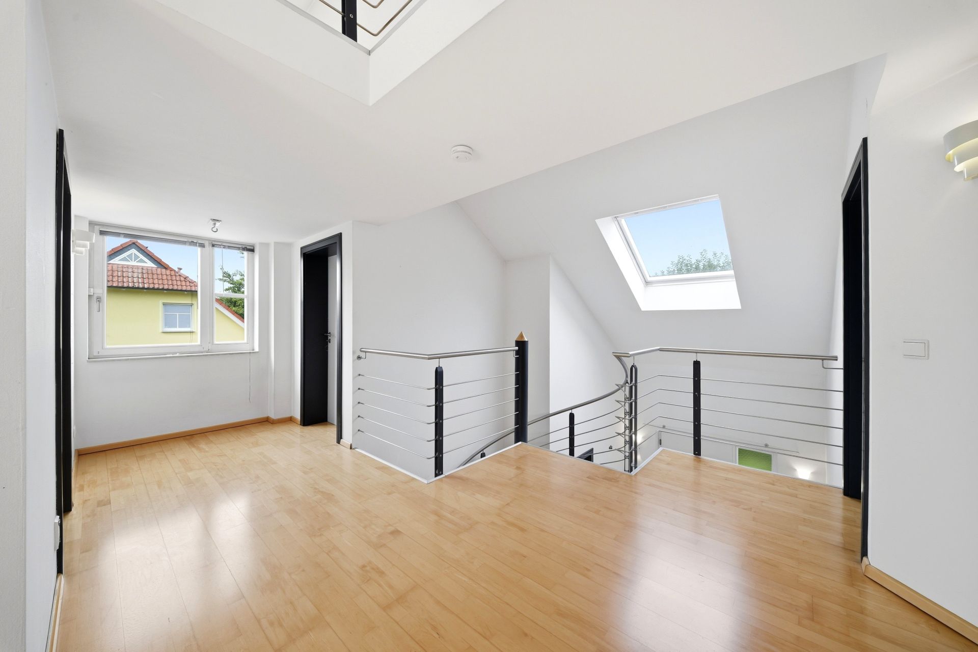 Heller Flur mit Holzfußboden, Fenstern und Metallgeländer im Obergeschoss eines Hauses.