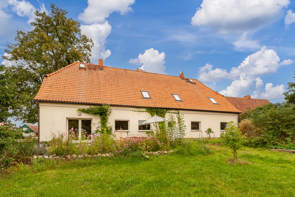 Großes weißes Wohnhaus mit rotem Dach, Garten und Sonnenschirm im Vordergrund.