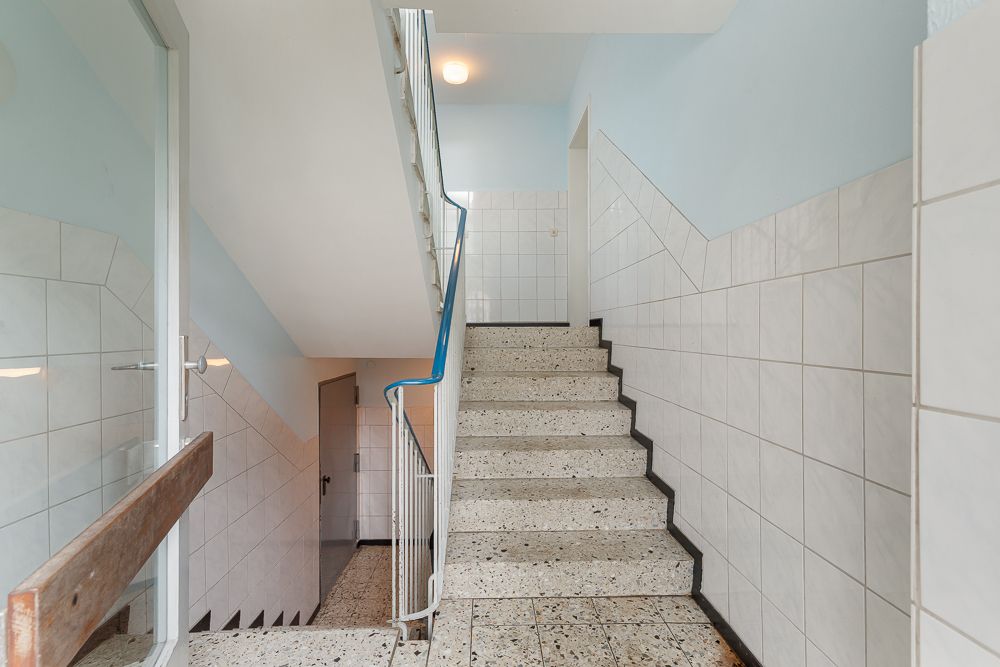 Helles Treppenhaus mit gefliestem Wänden und Terrazzo-Stufen in einem Wohnhaus.