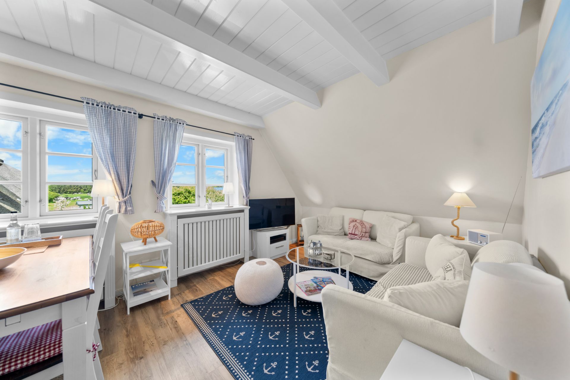 Helles Wohnzimmer mit zwei Sofas, Teppich, Fernseher, Fenstern mit Vorhängen und Holzbalkendecke.