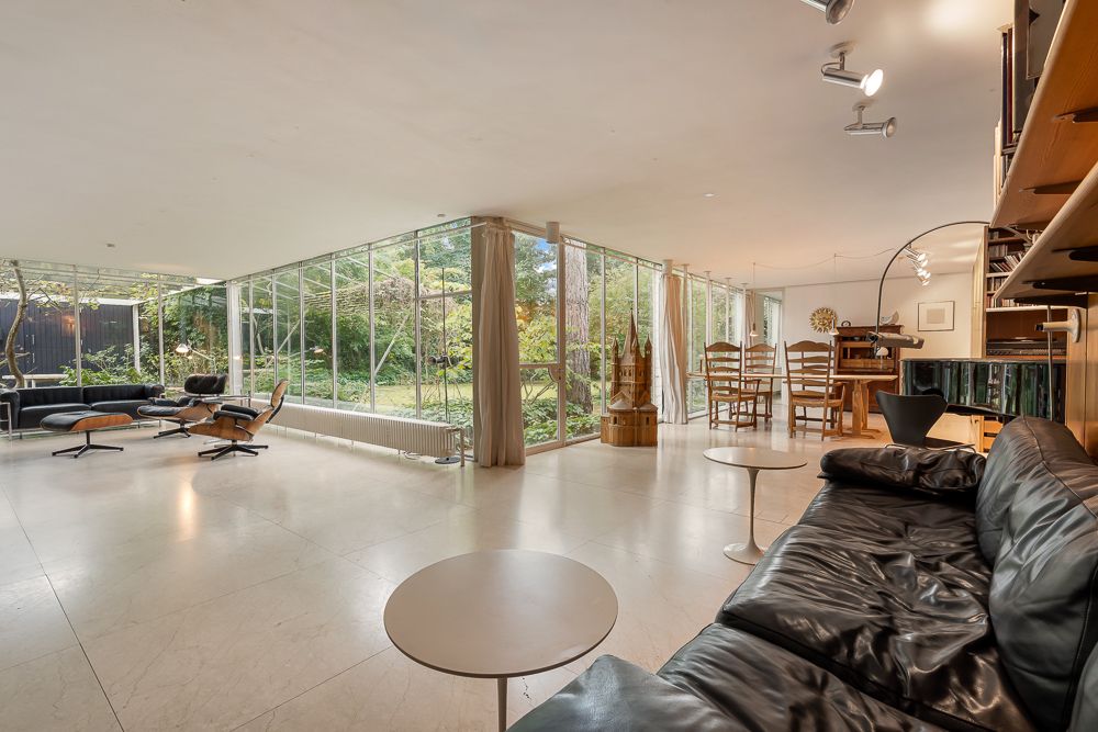 Helles Wohnzimmer mit großen Glasfenstern, schwarzem Sofa und Essbereich, Blick auf den Garten.