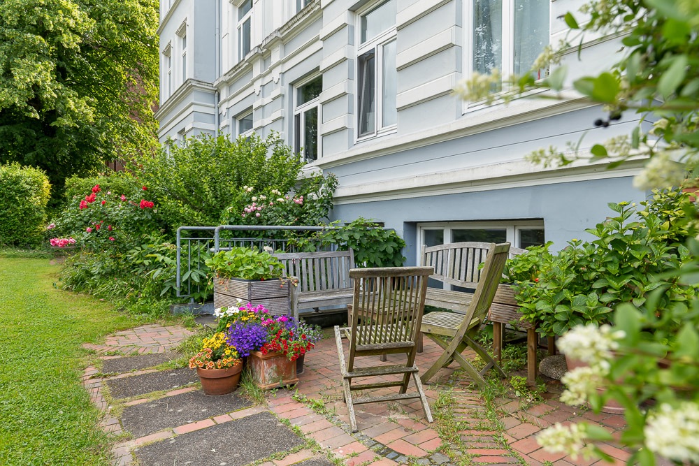 Kleine Terrasse mit Holzmöbeln und Blumen vor einem Wohnhaus.