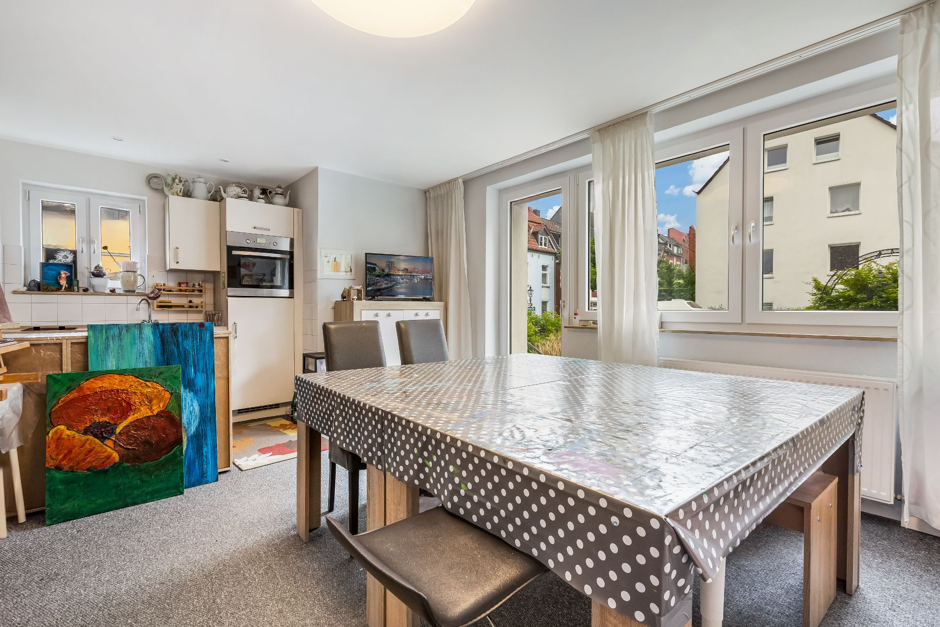 Heller Essbereich mit großem Fenstern, Esstisch mit gepunkteter Tischdecke und Blick in die Küche.