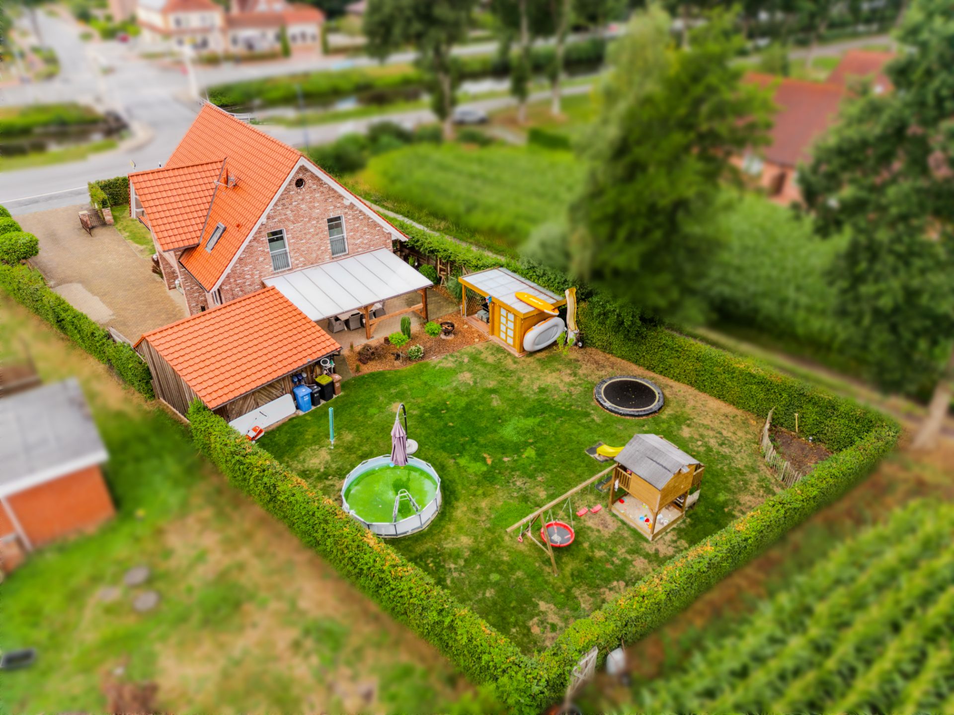 Luftaufnahme eines Einfamilienhauses mit Garten, Pool, Trampolin und Spielgeräten.