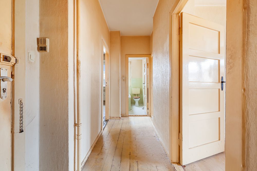 Heller Flur mit Holzboden und weißen Türen, im Hintergrund ein Badezimmer mit Toilette.
