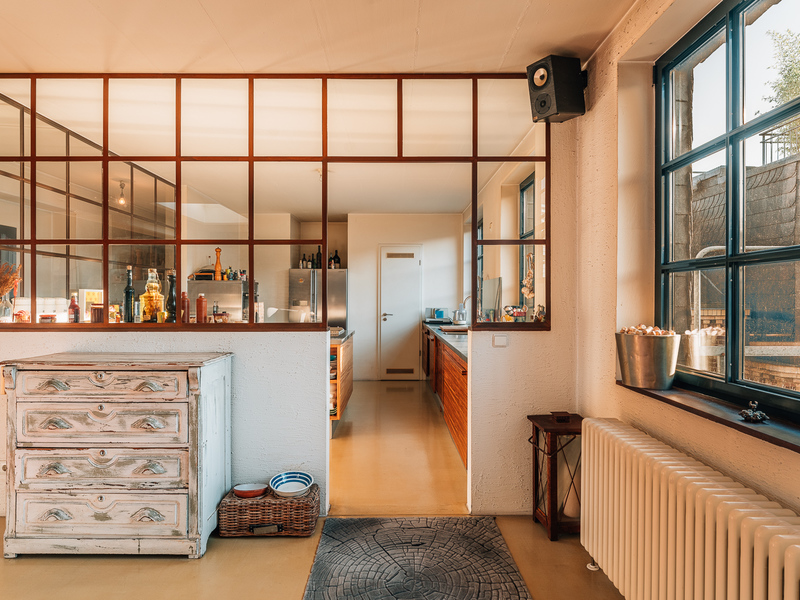 Helle Küche mit großen Fenstern, Glastrennwand, alten Kommoden und Heizkörper am Fenster.