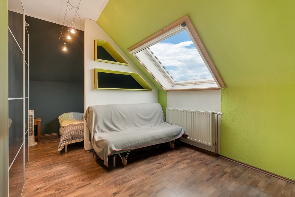 Helles Zimmer mit Dachschrägen, Schlafsofa, großem Fenster und Holzboden.