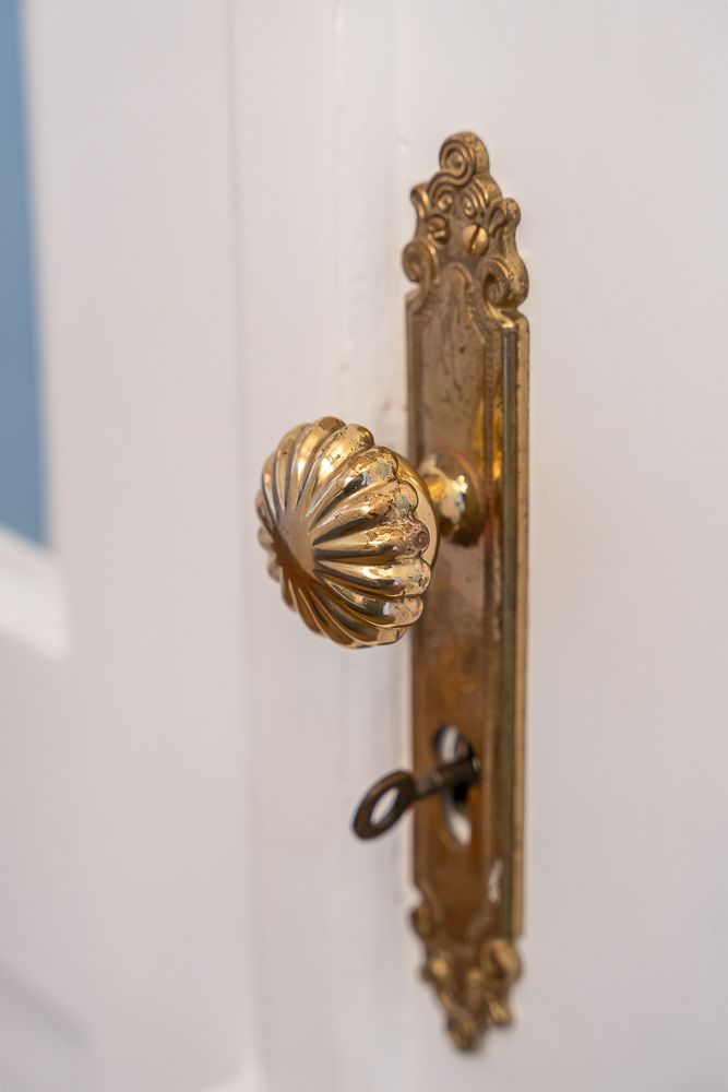 Nahaufnahme eines goldenen, verzierten Türgriffs mit Schlüssel in einer weißen Tür.