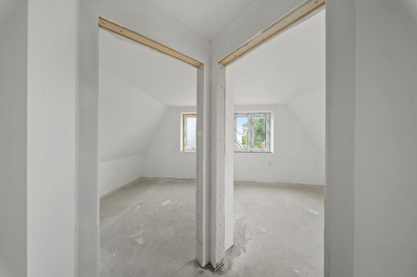 Zwei unfertige, helle Zimmer mit Fenstern und weiß gestrichenen Wänden, getrennt durch eine Wand.
