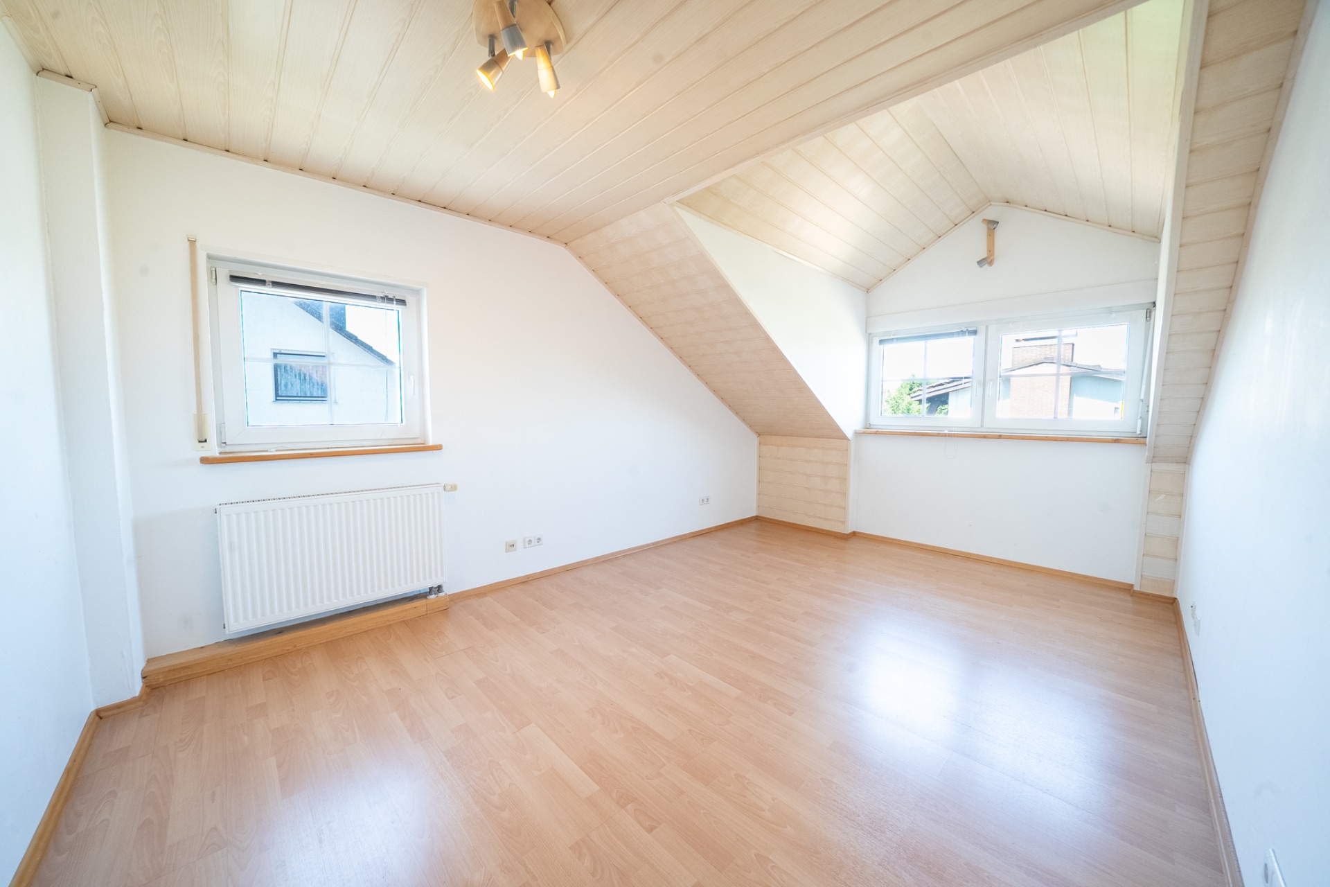 Helles Dachzimmer mit Holzdecke, Laminatboden und zwei Fenstern.