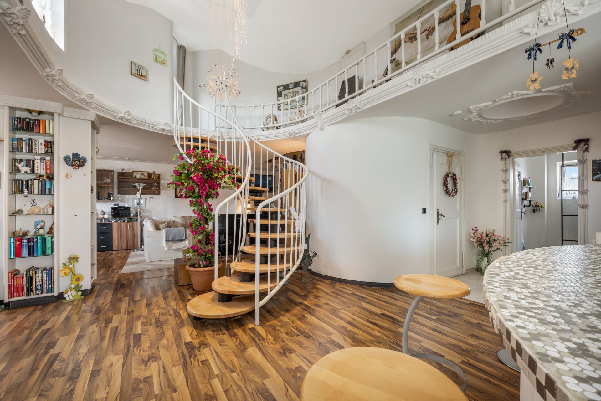 Helles Wohnzimmer mit Wendeltreppe, Holzboden, Bücherregal und runder Küchenbar.