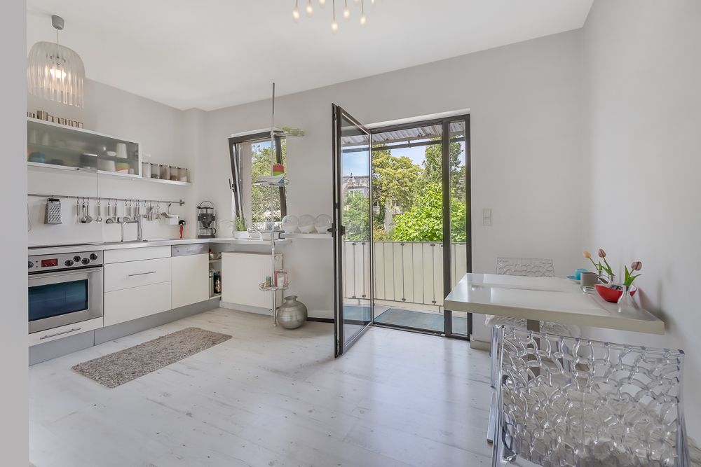 Helle moderne Küche mit Esstisch, offenem Fenster und Zugang zu einem Balkon.