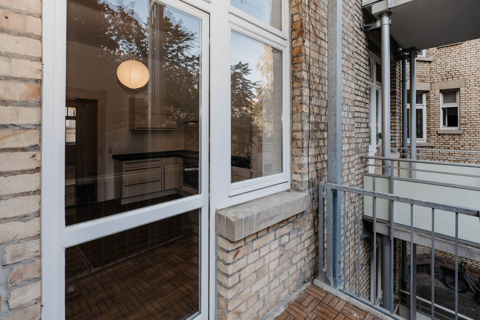 Balkon mit Blick auf große Fenster und Backsteinfassade, Innenraum mit Lampe sichtbar.