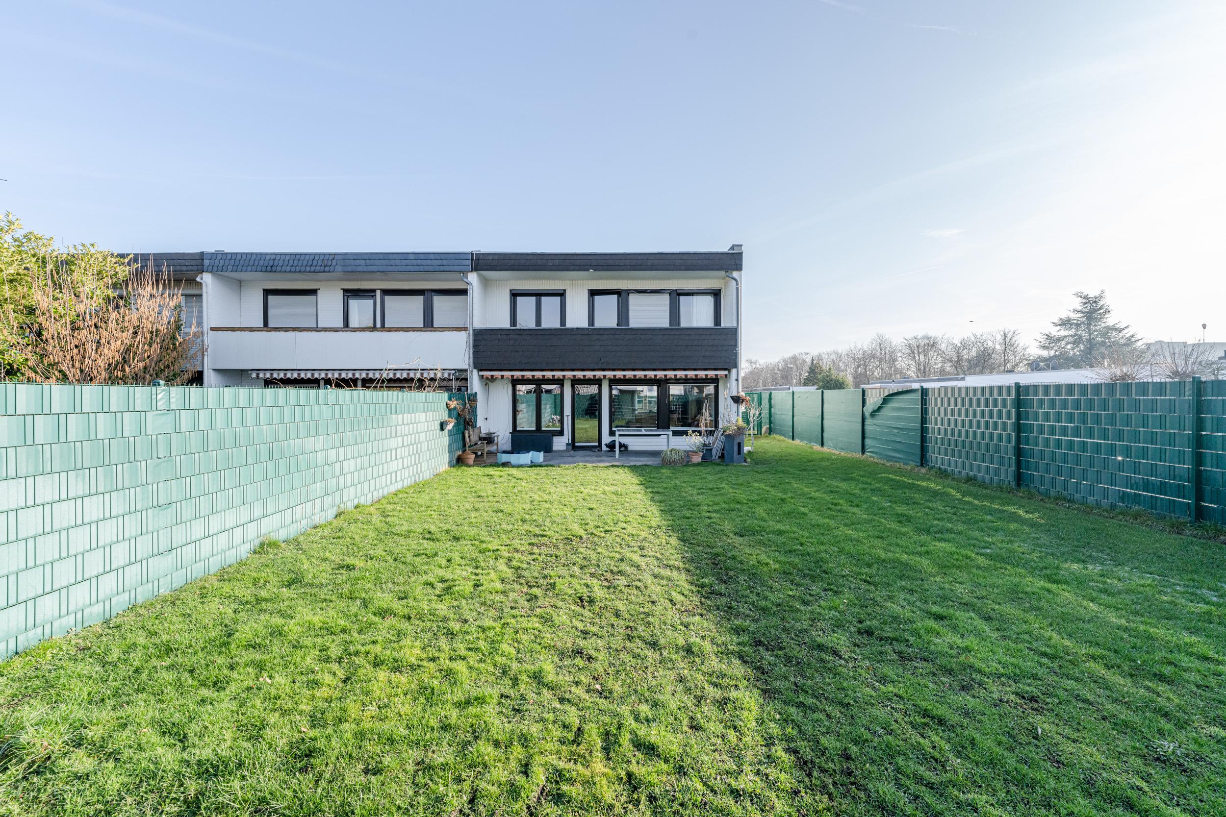 Rückseite eines Doppelhauses mit großem, eingezäuntem Garten und Terrasse.