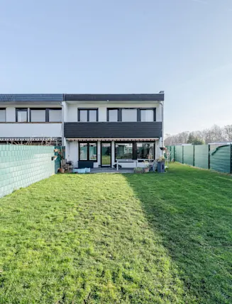 Rückseite eines Doppelhauses mit großem, eingezäuntem Garten und Terrasse.