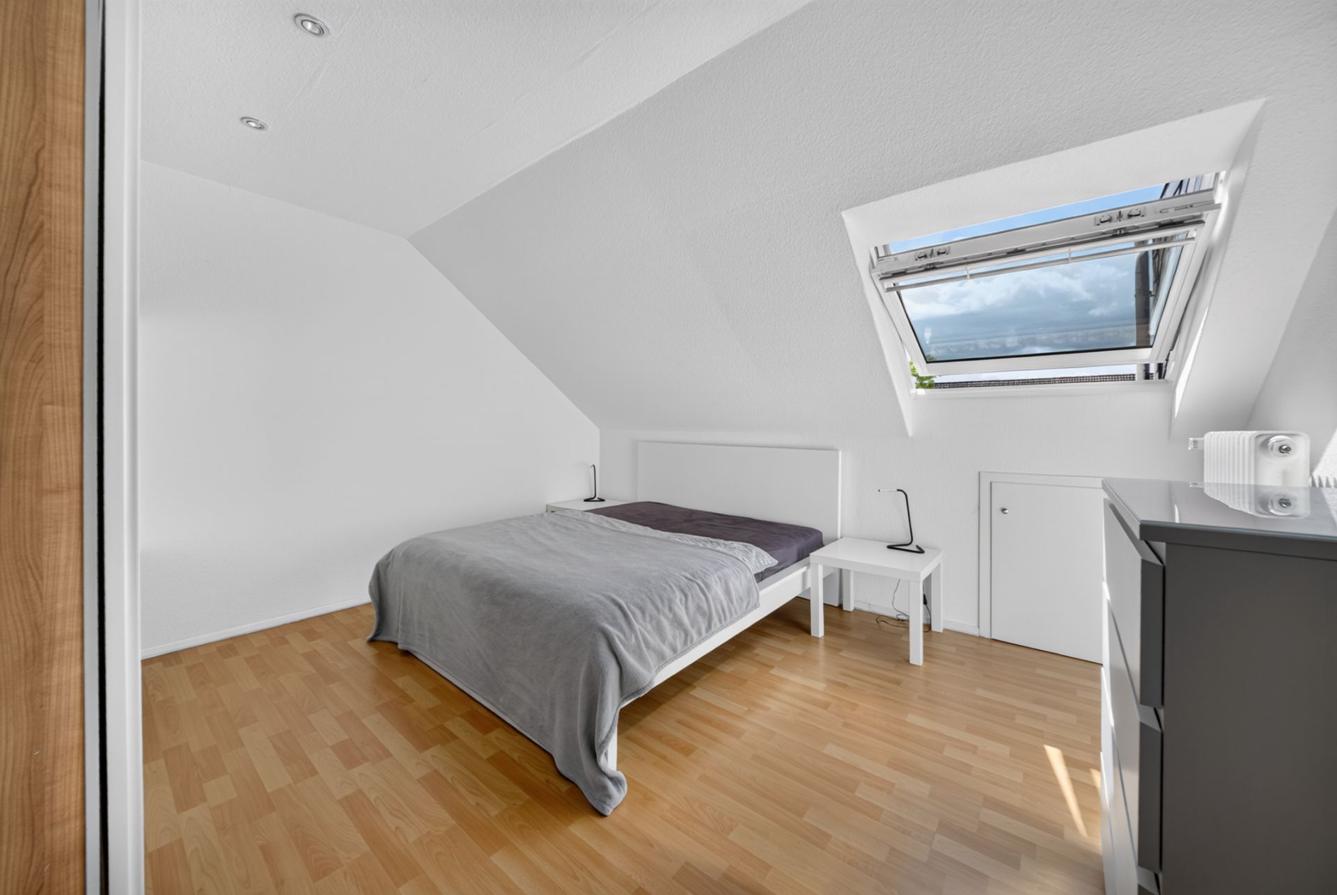 Helles Schlafzimmer mit Doppelbett, Nachttischen und Dachfenster unter einer Schräge.