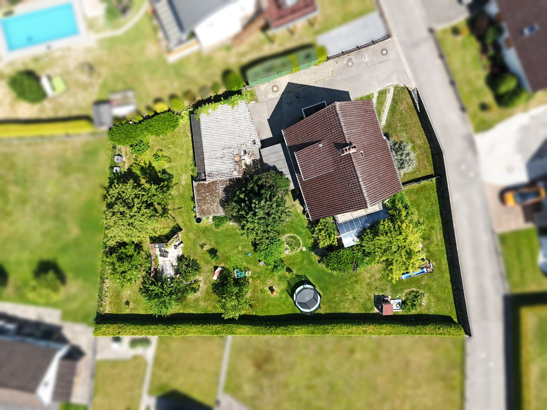 Luftbild eines Hauses mit großem Garten, Bäumen und Spielgerät, von Hecke umgeben.