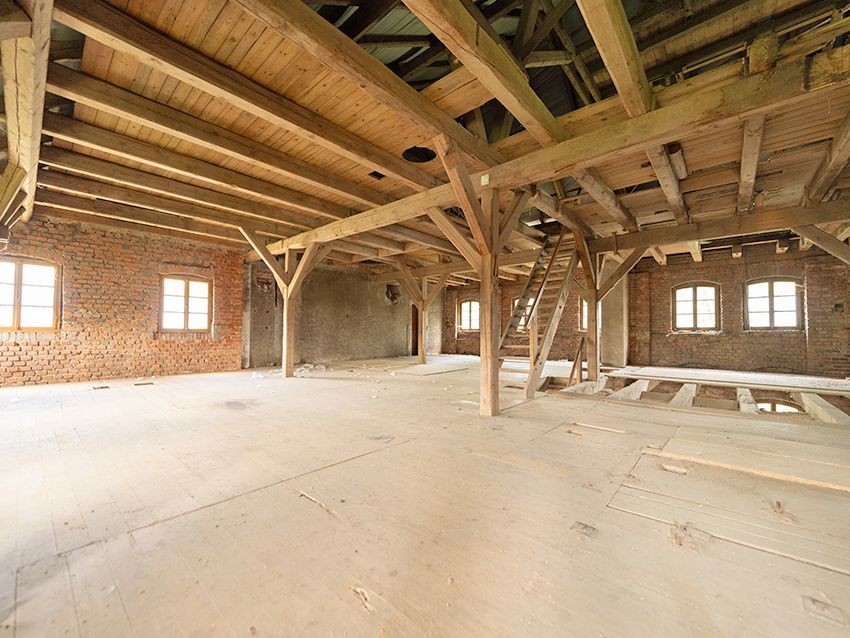 Großer, leerer Dachboden mit Holzbalken, Holzboden und Backsteinwänden.