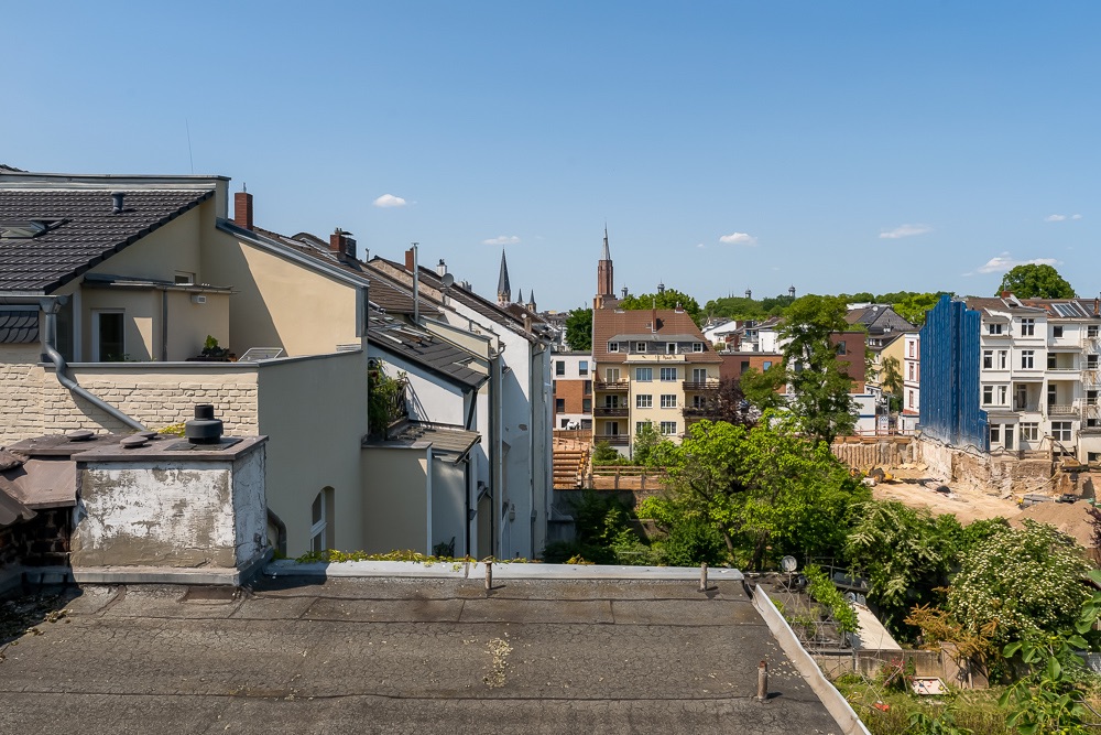 Blick auf Wohnhäuser und Baustelle unter blauem Himmel, Bäume im Vordergrund.
