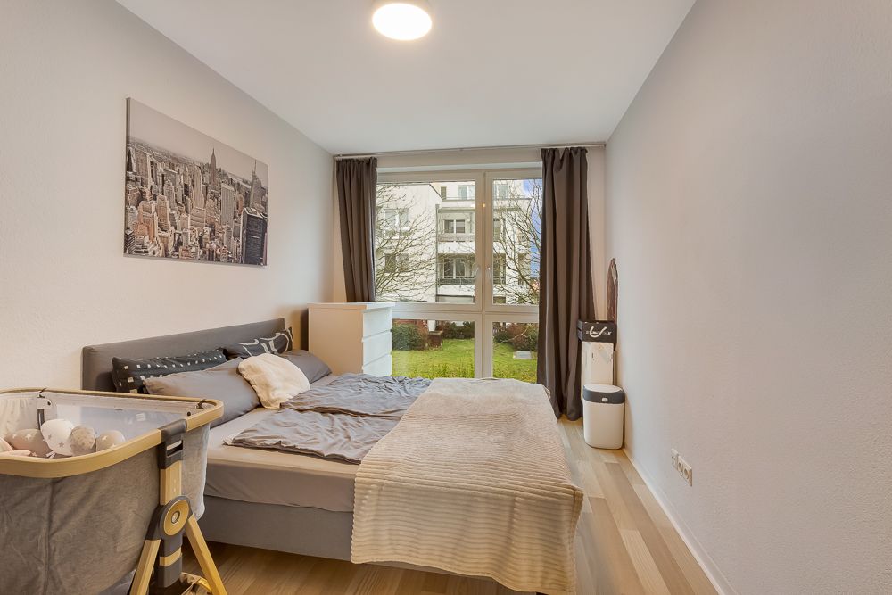 Schlafzimmer mit Doppelbett, Babybett, Kommode und großem Fenster mit Blick ins Grüne.