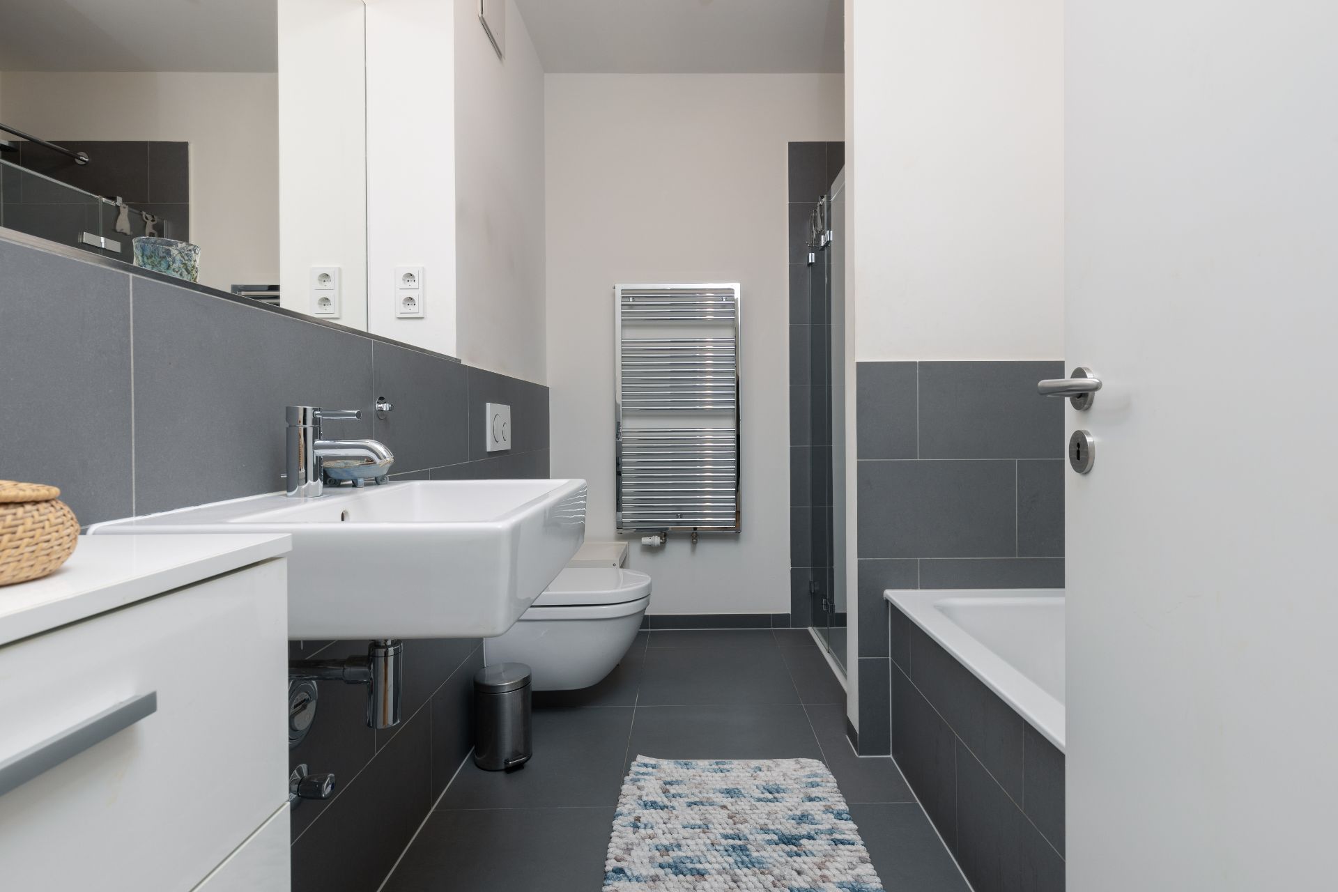 Modernes Badezimmer mit Waschbecken, Toilette, Badewanne und Handtuchheizkörper.