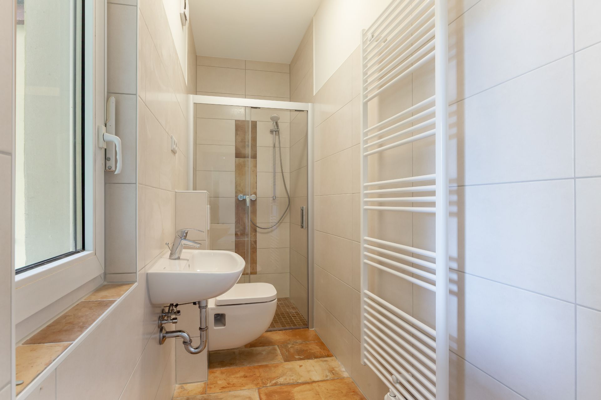 Helles Bad mit Fenster, Waschbecken, Toilette, Dusche und weißem Handtuchheizkörper.