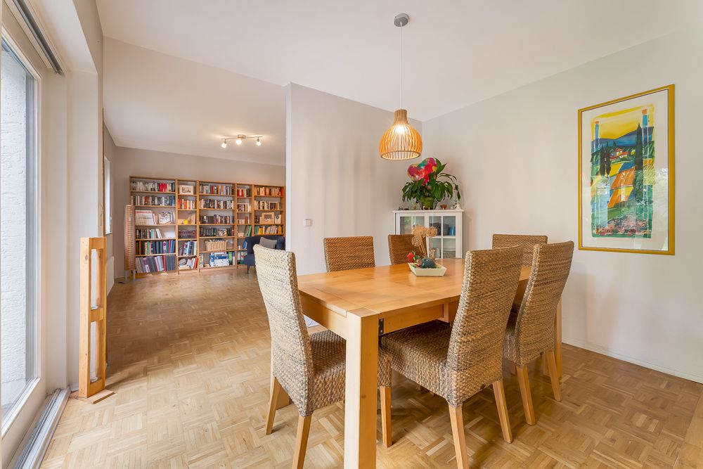 Essbereich mit Holztisch und sechs Stühlen, Bücherregal im Hintergrund, Parkettboden.