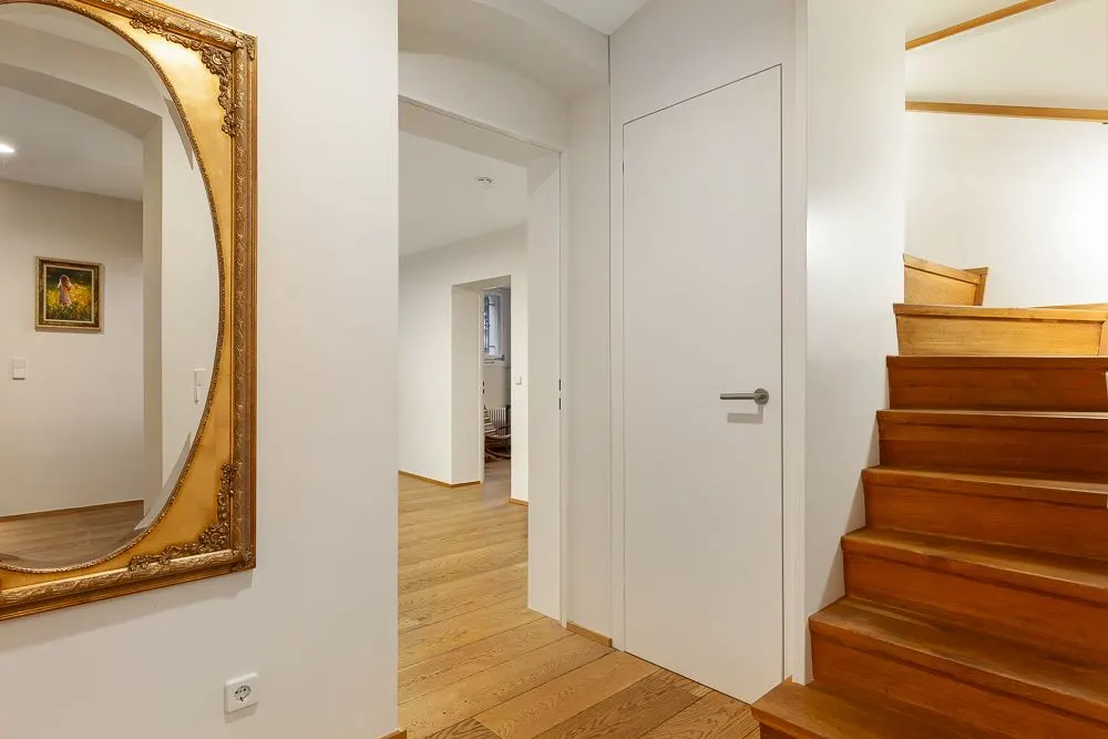 Heller Flur mit Holztreppe, großem Spiegel und Holzboden.