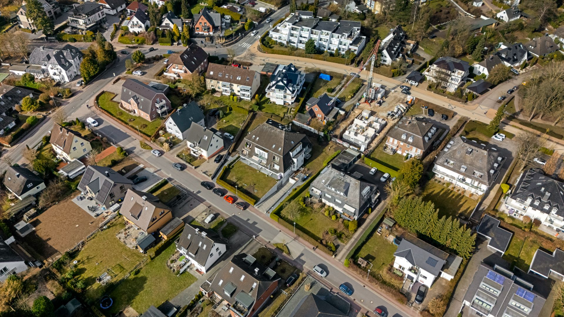 Luftaufnahme eines Wohngebiets mit mehreren Einfamilienhäusern, Straßen und grünen Gärten.