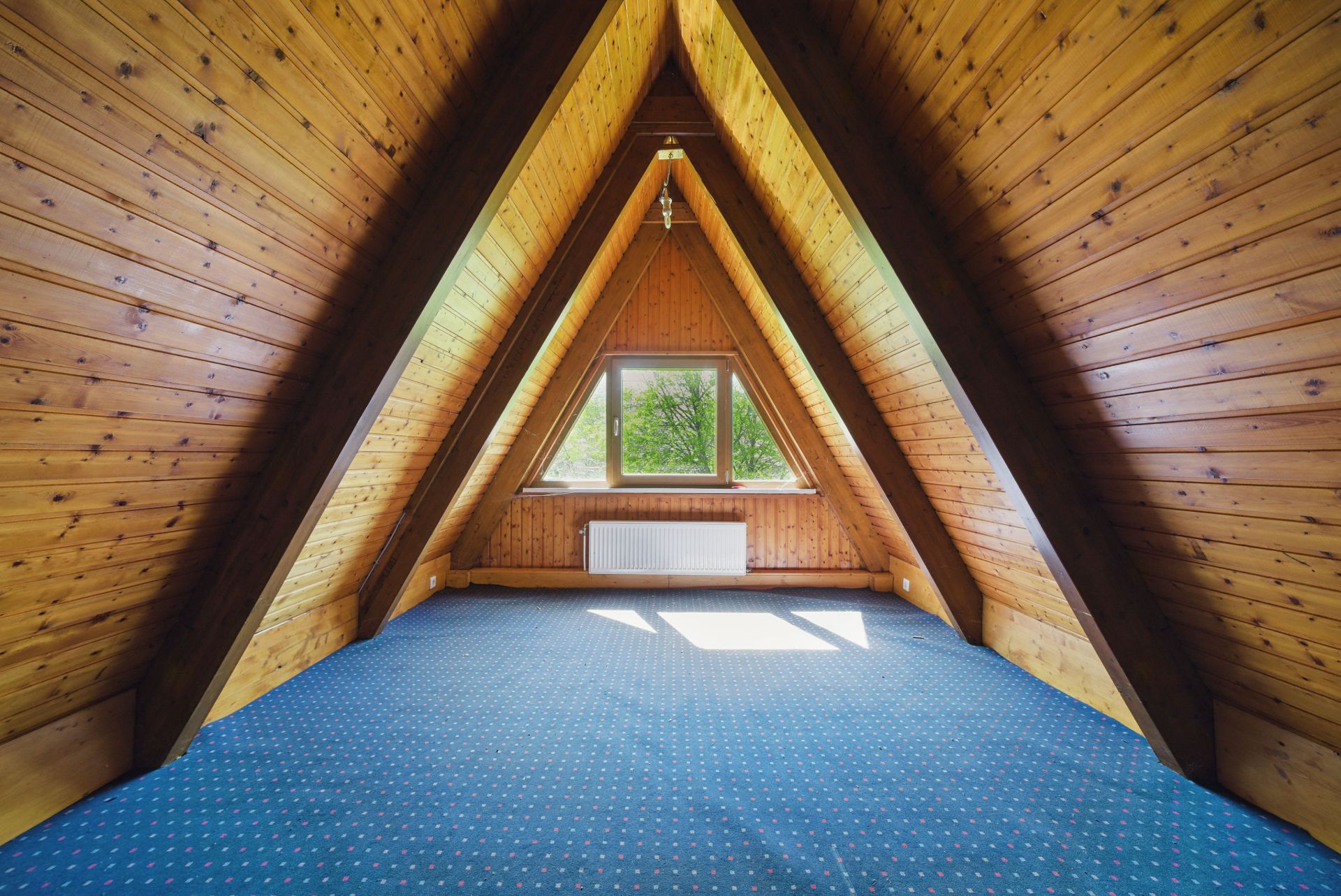 Dachgeschosszimmer mit Holzverkleidung, blauem Teppich und Fenster mit Blick ins Grüne.