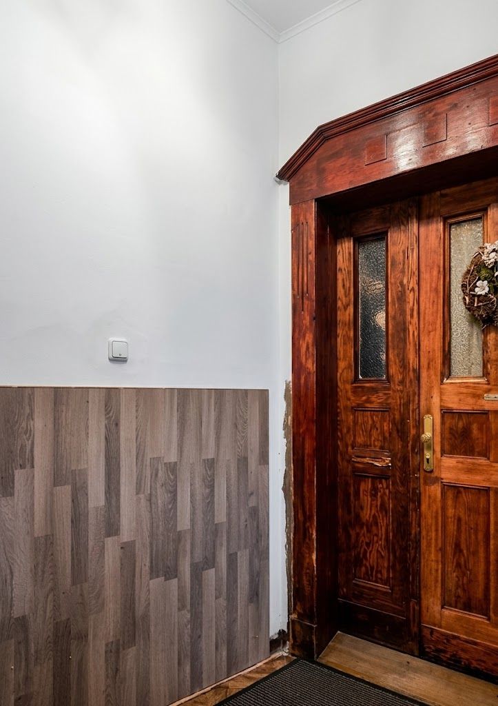 Holztür mit Glaseinsätzen und Kranz neben Wand mit Holzverkleidung.