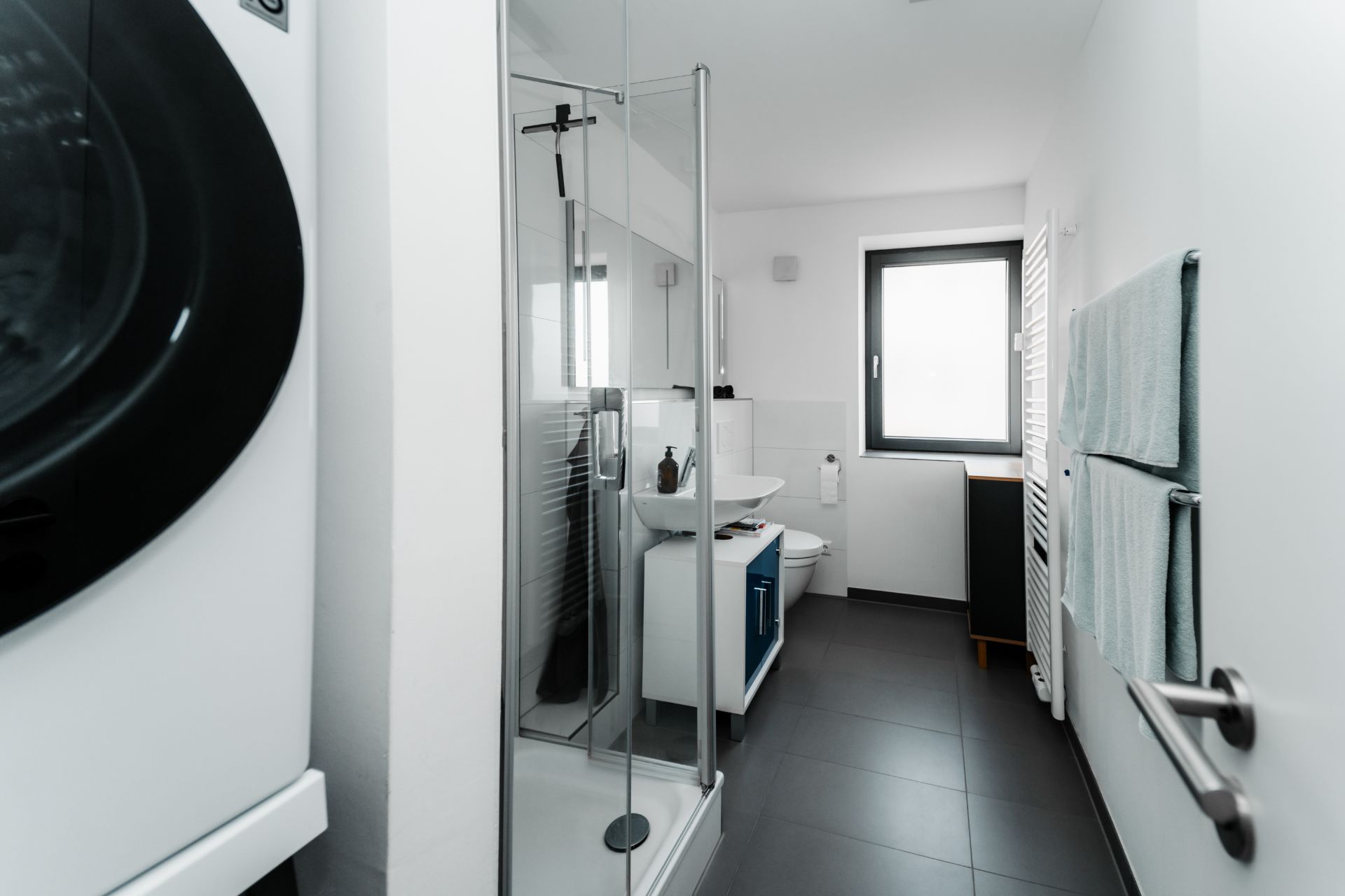 Modernes Badezimmer mit Dusche, Waschmaschine, Waschbecken und Fenster.