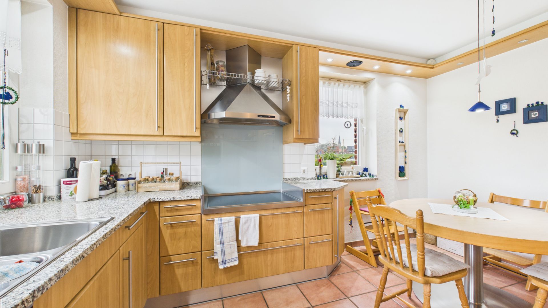 Helle Küche mit Holzmöbeln, Esstisch und Fenster, ansprechende Dekoration und moderne Geräte.
