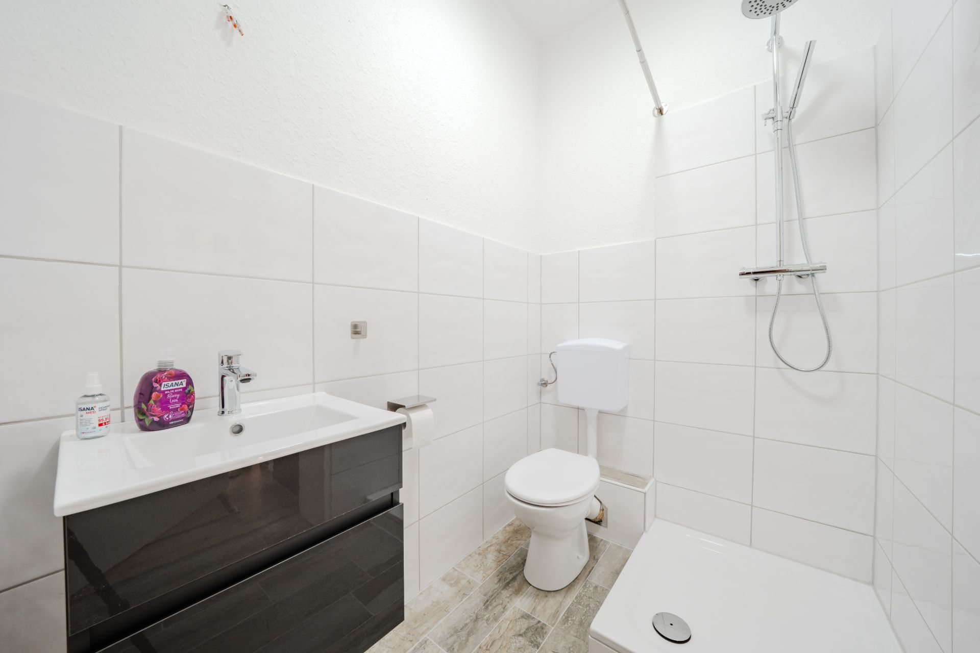Modernes Badezimmer mit Waschbecken, Toilette und offener Dusche auf Fliesenboden.