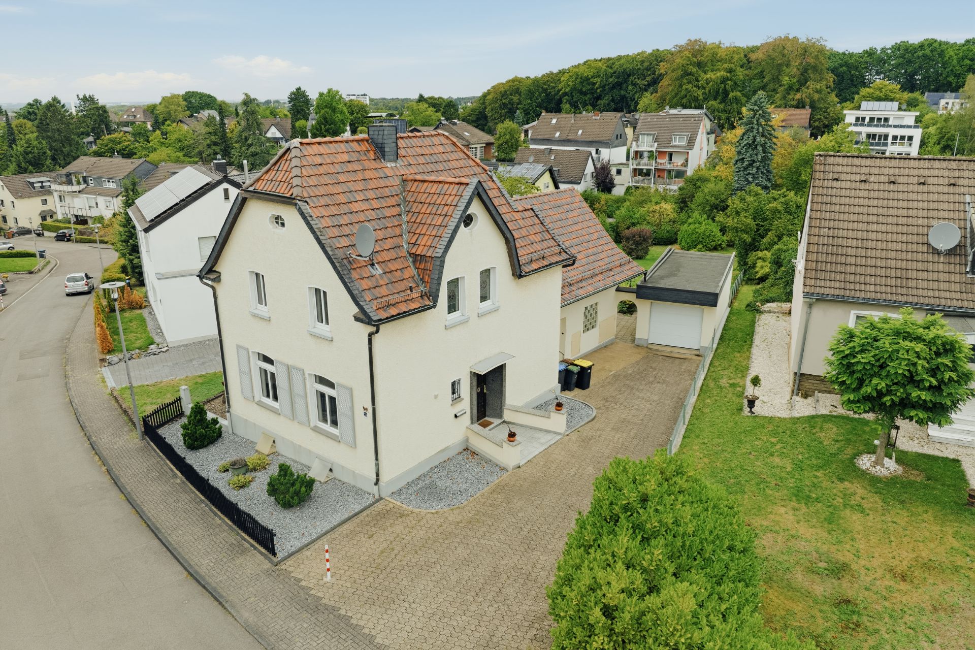 Freistehendes Wohnhaus mit rotem Dach, gepflasterter Einfahrt und kleinem Garten, in ruhigem Wohngebiet.