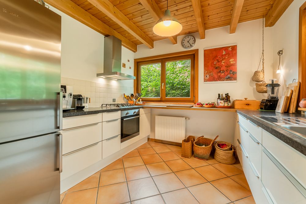 Moderne Küche mit Holzdecke, weißen Schränken, großem Fenster und Körben auf dem Boden.