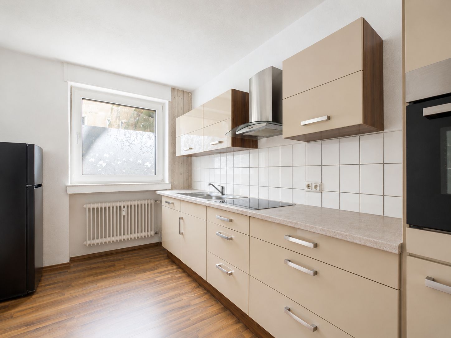 Moderne Einbauküche mit Herd, Spüle, Ober- und Unterschränken und großem Fenster.