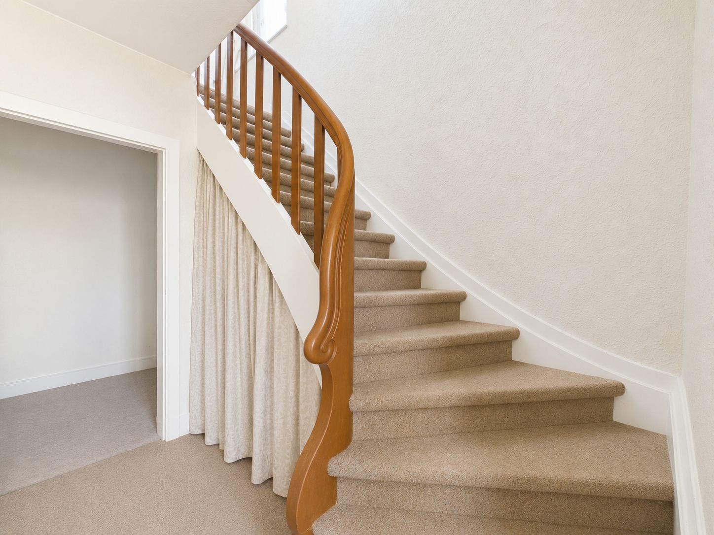 Treppe mit Holzgeländer und beigem Teppichboden, daneben ein leerer Raum.