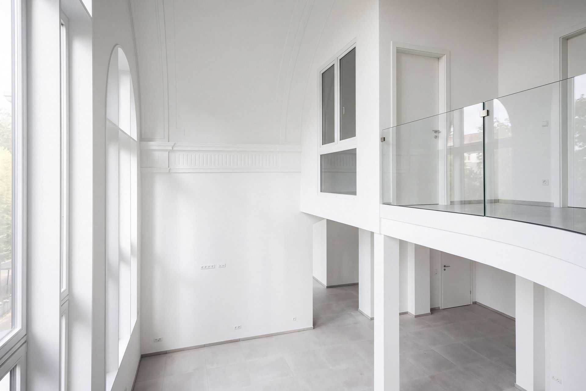 Heller Wohnraum mit hohen Decken, großen Fenstern und einer Galerie mit Glasgeländer.