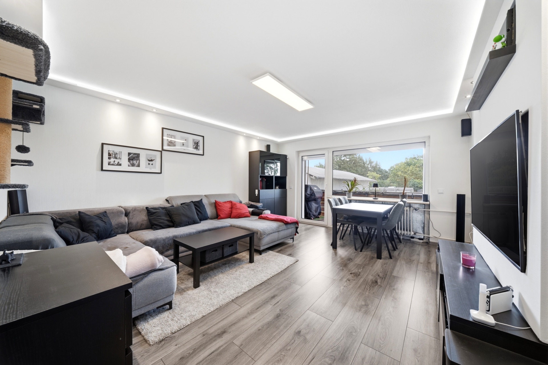 Modernes Wohnzimmer mit Ecksofa, Esstisch, großem Fenster und Fernseher.