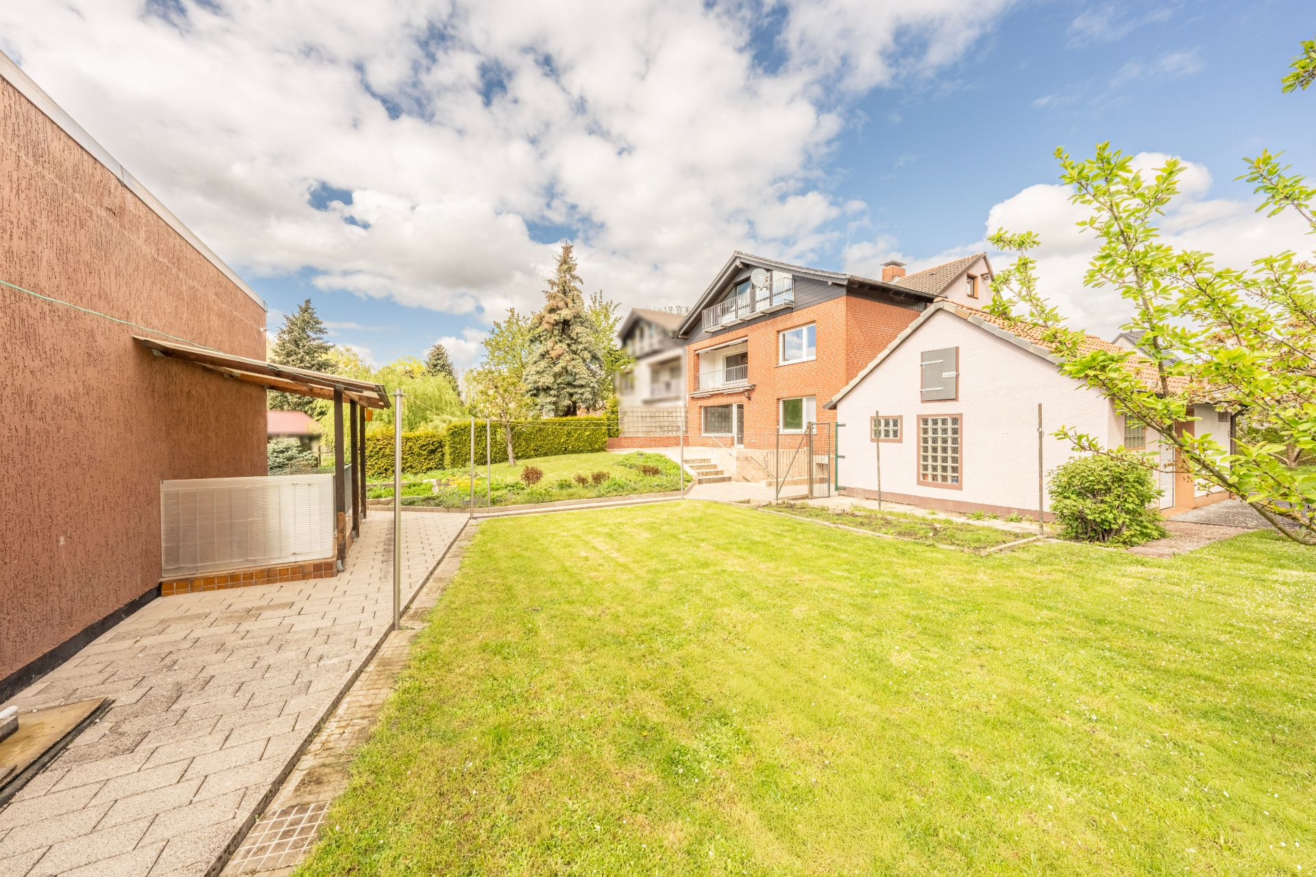 Zweistöckiges Wohnhaus mit Garten, Terrasse und Rasenfläche an einem sonnigen Tag.