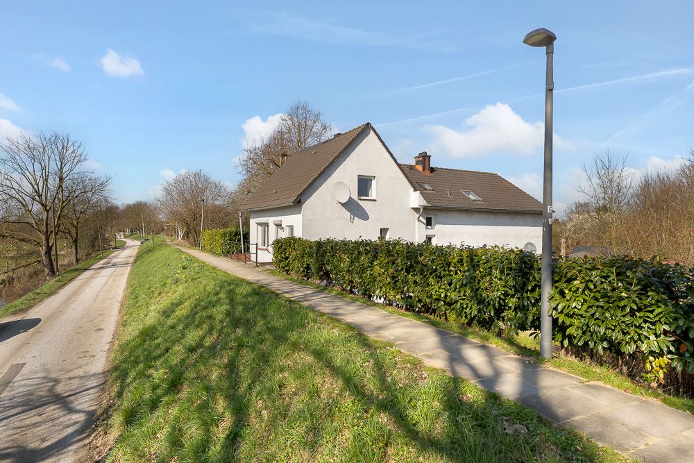 Weißes Einfamilienhaus mit Gartengrün an einer ruhigen Straße, Laterne und Gehweg im Vordergrund.